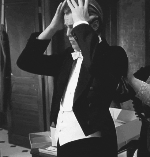 Movie gif. Leonardo DiCaprio as Jack in Titanic. He has a tuxedo on and is looking fresh. Jack uses both hands to slick his hair back, putting the final touches on.