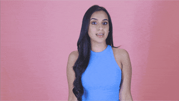 Video gif. A young woman points at herself, then at us, and then makes a heart with her hands.