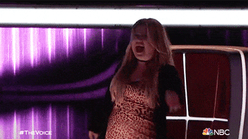 Reality TV gif. Kelly Clarkson on "The Voice" standing up from her judge seat and dancing during a performance.