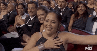 Video gif. Jharrel Jerome's mother in the audience at the Emmys touches her hand to her heart and then points out with pride, as others around her applaud.