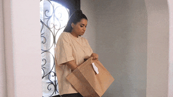 Video gif. Lilly Singh, a Youtuber, picks up the delivery from her doorstep. She pauses in the doorway and shoves a handful of fries in her mouth before heading into the house.