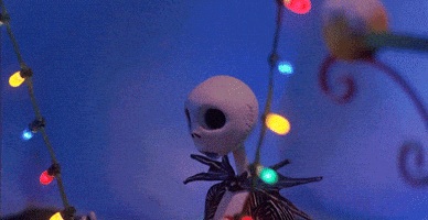 Stop motion gif. Jack Skellington, in festive silliness, puts Christmas lights up to his face as if the are his eyes.