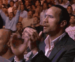 Celebrity gif. Dwayne Johnson chomps on gum and stands in a crowd. He shakes his head with an amazed expression, clapping his hands like he's impressed.