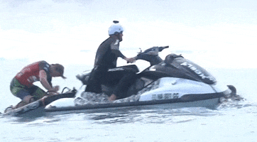 Sports gif. A big wave surfer dressed in competition gear is on the rescue board on the back of a jetski and he's punching it angrily. His surfboard is nowhere to be seen.