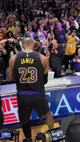 Sports gif. The back of Lebron James of the Los Angeles Lakers wears his basketball jersey, tossing white powder in the air to create what looks like a cloud of white smoke in front of a stadium full of fans watching him. 
