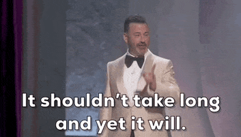Oscars 2024 GIF. Jimmy Kimmel has changed suit jackets and is now rocking a shiny beige suit over a white shirt and black tie. He points his index finger at us and the audience and declares, "It shouldn't take long and yet it will."