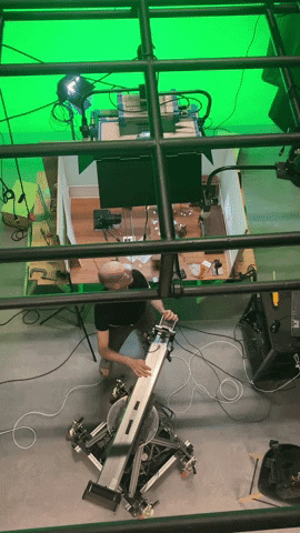 Video gif. Man looks up into the rafters of a movie set.