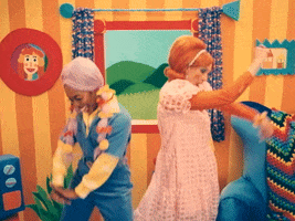 TV gif. Two characters in "Happy Place" wearing orange and lavender wigs stand back to back and do awkward dorky dance moves that look like they are trying to be sexy in front of a bright cartoonish living-room set. 