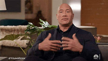 TV gif. Dwayne Johnson as The Rock on Young Rock, shrugs with his arms at his sides, smiling  at us with a chuckle. 