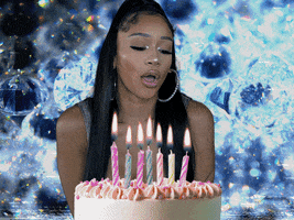 Video gif. Saweetie sitting in front of a birthday cake that appears and disappears from the bottom of the screen. She slowly blows across the line of candles in a seductive way, then winks at us against a swirling background filled with diamond gemstones. Text appears, "Happy Birthday." 