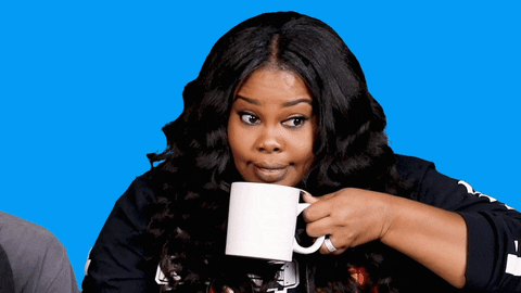 Celebrity gif. Actress Amber Riley sits and holds a mug close to her face. Her eyes are big as she looks around like she just heard or said something she shouldn't have then takes a sip of her drink.