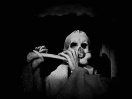 Video gif. Black and white close-up of a spooky skeleton playing a human femur bone like a flute, its bony fingers moving expertly.