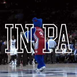 Sports gif. The mascot for the Philadelphia 76ers throws a basketball behind him without looking, making the basket as people in the crowd cheer. Text, “In PA we don’t miss an election.”