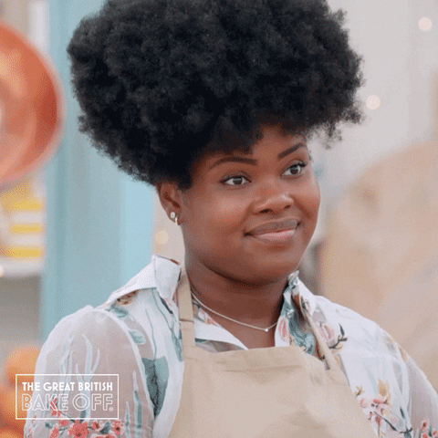 Reality TV gif. A contestant from the Great British Bakeoff gives a light smile and two thumbs up.