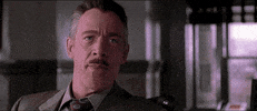 Movie gif. J.K. Simmons as J. Jonah Jameson in Spiderman laughs hysterically as Toby Maguire as Peter Parker stares at him confused and offended. Bill Nunn as Robbie Robertson sits next to Peter and shakes his head, irritated by Jameson’s laughing.
