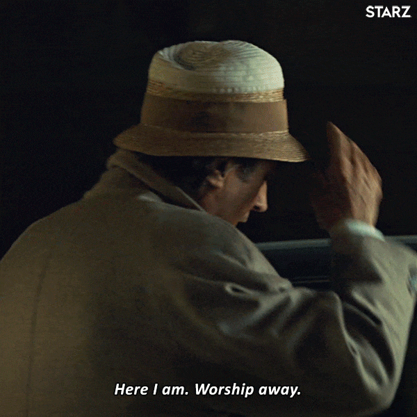 TV gif. Ian McShane as Odin on American Gods turns around while taking his hat off. He holds his arms out to present himself as he says, “Her I am. Worship Away.”