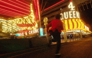 Music video gif. From the video for "Heartless", The Weeknd runs frantically past bright casino entrances wearing sunglasses and a pink jacket.