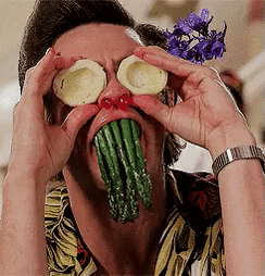 Movie gif. Jim Carrey as Ace Ventura holds asparagus in his mouth as if they were teeth and potatoes as eyes then blows red cherries out of his nostrils.