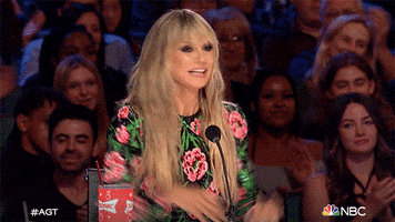 Reality TV gif. Heidi Klum as a judge on America's Got Talent. She raises her arms above her head and shouts, "Yes!"