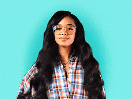Celebrity gif. H.E.R. smiles and waves, wearing an oversize plaid button-down and standing in front of a turquoise background.