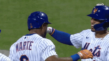 Sports gif. Slow motion video of Francisco Lindor and Jeff McNeil from the New York Mets smiling proudly and coming in for a big hug on the field.