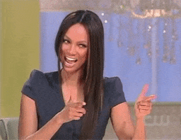 Celebrity gif. Tyra Banks exaggeratedly winks and smiles at someone. She holds up two finger guns and shoots them at someone.