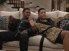TV gif. Alfonso Ribeiro and Will Smith as Carlton and Will in The Fresh Prince of Bel-Air, sit on the couch next to each other in their pajamas. Carlton moves his hands up and down and rocks back and forth, while Will spins his hands around and wiggle-dances next to him, singing or rapping. 