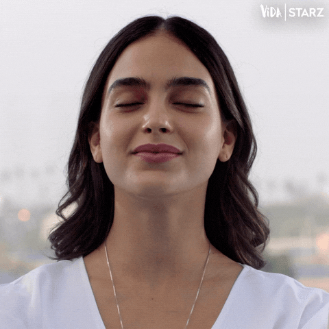 TV gif. Dressed in white, Melissa Barrera as Lyn from Vida smiles slightly and gulps, eyes closed.