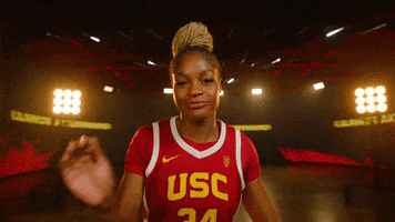 Promo gif. Clarice Akunwafo, a USC women's basketball player swipes at the camera and gives a sassy look as she turns around to walk away. Behind her is a set with stage lights and giant floor-to-ceiling curved TVs. 