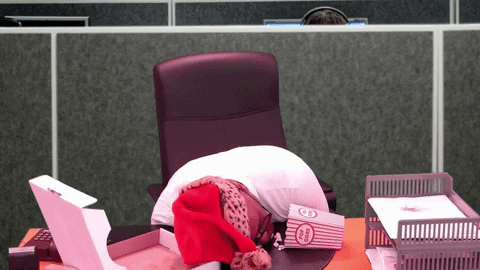 Probouzející se muž s čepicí Santa Clause, sedící za stolem v kanceláři na vánočním večírku. 