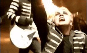 Music video gif. From My Chemical Romance's video for Famous Last Words, Gerard Way holds his arm up in the air, looking up pleading while singing, as guitarists play their instruments in a fiery background.