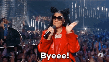 Video gif. Nicki Minaj at the 2023 VMAs, wearing dark oversized sunglasses and a red leather jacket with her hair in half-up-half-down high buns, holding a microphone while smiling and waving at the crowd. Text, "Byeeee!'