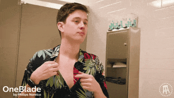 Ad gif. OneBlade by Philips Norelco ad, where a young man checks himself out in a bathroom mirror, holding his shirt collar out, touching his finger to his tongue then placing his finger on his bare chest as he looks at us and snarls.
