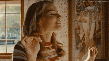 Movie gif. Margot Robbie as Sharon Tate in Once Upon a Time in Hollywood smiles as she dances with her eyes closed and her hands up.