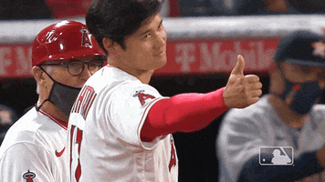 Sports gif. Shohei Ohtani wears a Washington Nationals uniform as he walks in slow motion. He holds out a big thumbs up with a cocky look on his face.
