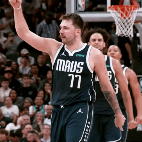 Sports gif. Luka Doncic of the Dallas Mavericks is on the court and he's grinning while he points down at his chest and then raises his fist back in the air. 