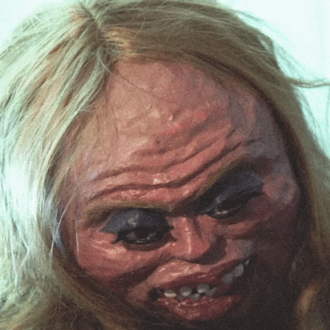 Video gif. A giant, scary paper mache mask of a blonde woman with wrinkles and rotting teeth.