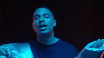 Music video gif. Arin Ray in his video for A Seat bobs and sways as he sings in the dark.