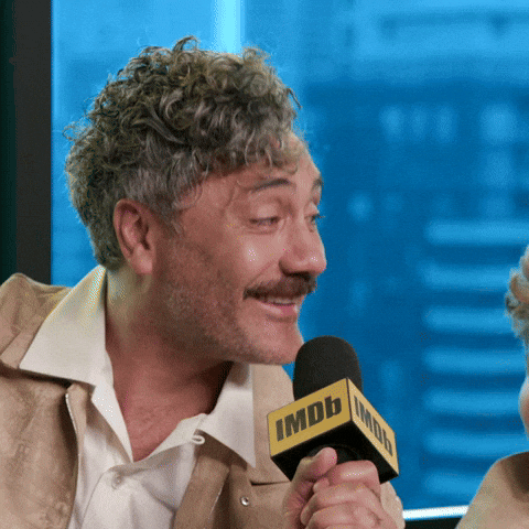 Celebrity gif. Taika Waititi leans into a microphone and nods in agreement, laughing and smiling as he speaks into the mic. He says, ‘You're right.”