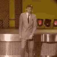 TV gif. A man with a mullet and a gray suit, dances on a show that looks like it's from the 1980s. He moves forward, jerking his bent arms and legs around awkwardly as he takes his time dancing in a circle.