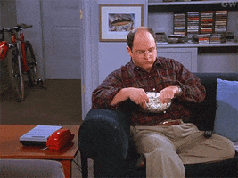 Seinfeld gif. Jason Alexander as George contentedly shrugs while snacking on popcorn.