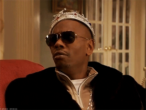 TV gif. A worried Dave Chappelle, wearing sunglasses and a crown, clutches stacks of money to his chest.