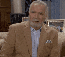 TV gif. John McCook as Eric Forrester in The Bold and the Beautiful is decked out in a caramel-colored suit and applauds somebody from his sitting position on a gold-patterned sofa.