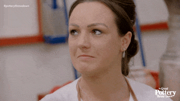 Reality TV gif. A contestant on the Great Pottery Throw Down grimaces and crosses her fingers on both hands, expecting the worst but hoping for the best.