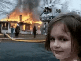Meme gif. A young girl looks at us over her shoulder with a devious smirk on her face. Behind a house is on fire and firefighters are in the front yard. 