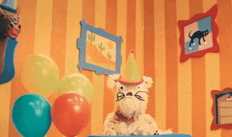 TV gif. Scruffy, a fluffy puppet dog, in "Happy Place" in a bright cartoon-style room wearing a birthday party hat and nodding its head, saying, "Happy birthday!'