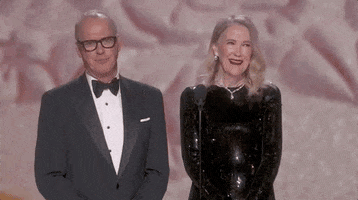 Oscars 2024 GIF. Catherine O'Hara and Michael Keaton stand at the podium, announcing the nominees for Best Makeup and Costume. O'Hara laughs and throws her head back, saying, "If I had a nickel!" 