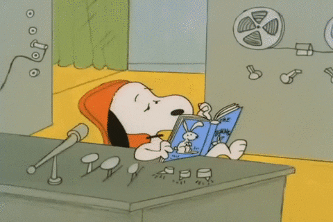 Snoopy, a beagle and character from a comic called Peanuts, is sitting at a desk reading a book. 