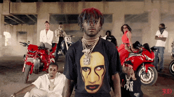 Music video gif. Push in on Lil Uzi Vert in the Bad and Boujee video, standing in front of a group of men and women on motorcycles as he shrugs his shoulders and smiles.