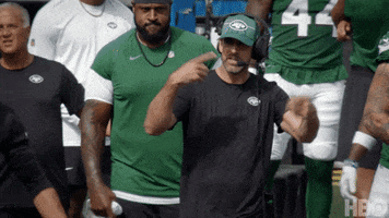Sports gif. Coach Aaron Rodgers stands on the sidelines wearing a New York Jets hat. He cycles his fingers forward like he's motioning to keep it rolling, then tosses his arms out wide like Let's go already." 